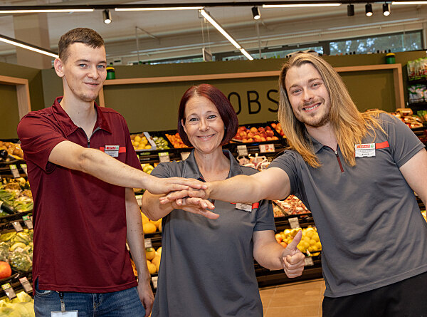 SPAR-Mitarbeiter:innen Fabian Stramitzer, Manuela Schornegg und Jürgen Pieber legen in einem Supermarkt ihre Hände übereinander.